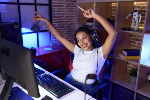 Young arab woman streamer playing video game with winner expression at gaming room