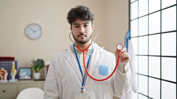 Jovem Hispânico Homem Médico Com Expressão Séria Segurando Estetoscópio Clínica — Fotografia de Stock