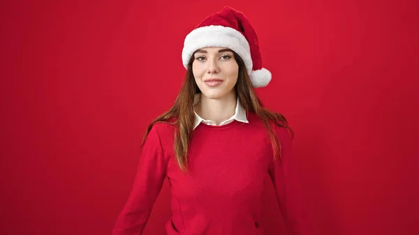 年轻的惊慌失措的女人带着自信的笑容 戴着圣诞帽 披着孤零零的红色背景 — 图库照片