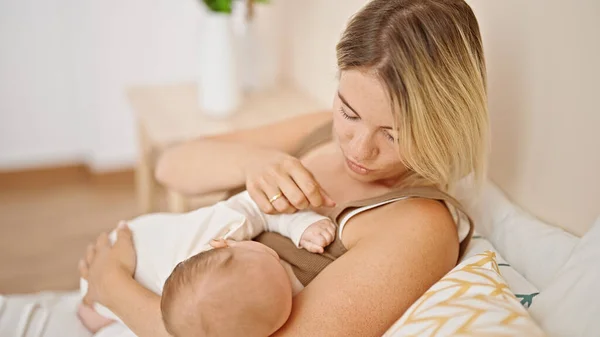 Mother and daughter sitting on bed breastfeeding baby at bedroom