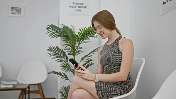 Bekleme Odasında Gülümseyen Akıllı Telefonu Kullanarak Sandalyede Oturan Genç Sarışın — Stok fotoğraf