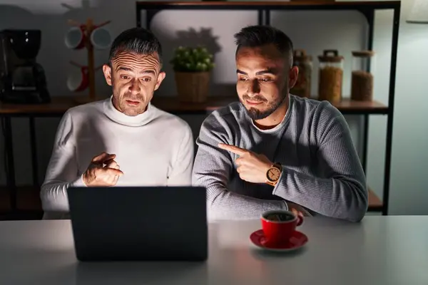Homosexual couple using computer laptop pointing aside worried and nervous with forefinger, concerned and surprised expression