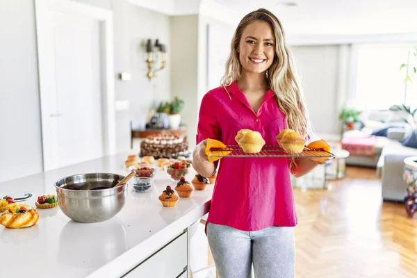 Mujer Joven Sonriendo Confiado Sosteniendo Bandeja Horno Con Cupcakes Cocina —  Fotos de Stock