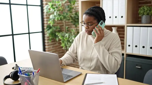 在办公室用手提电脑用智能手机聊天的非洲裔美国女商人 — 图库照片