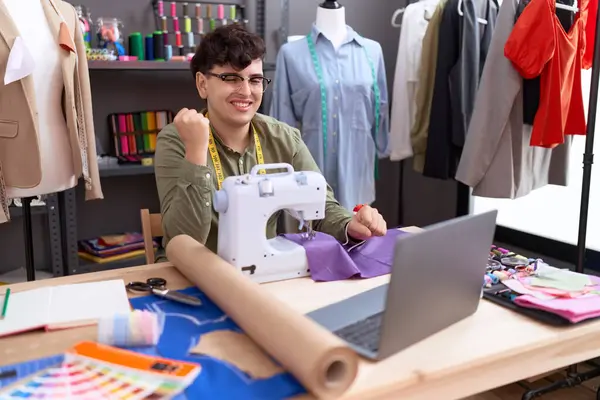 Young non binary man dressmaker designer on video call with laptop screaming proud, celebrating victory and success very excited with raised arm