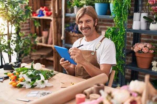 Young blond man florist smiling confident using touchpad at flower shop