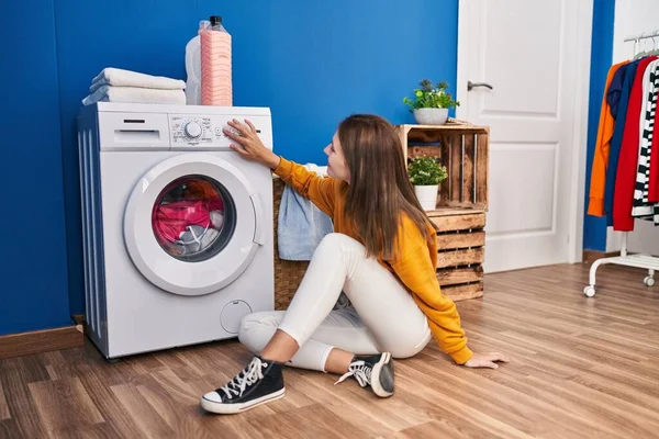 洗濯室で洗濯機を回す床に座っている若い金髪の女性 — ストック写真