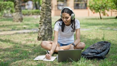 Laptop ve kulaklık kullanan Afrikalı Amerikalı bir kız öğrenci üniversite kampüsünde notlar alıyor.