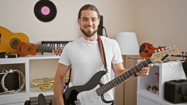 Genç İspanyol müzisyen gülerek müzik stüdyosunda elektro gitar çalıyor.