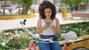 Parkta bankta oturan akıllı telefon kullanan genç, güzel İspanyol bir motorcu.