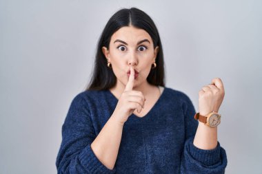 Genç esmer kadın izole edilmiş arka planda dikiliyor ve parmakları yana doğru uzanmış sessiz olmak istiyor. sessizlik ve gizli konsept. 