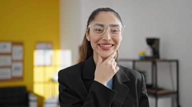 Genç, güzel, İspanyol bir iş kadını ofiste kendinden emin gülümsüyor.