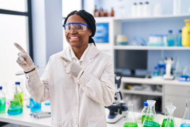 Afrika kökenli Amerikalı bir kadın bilim adamının laboratuvarında çalışıyor. Gülümsüyor ve kameraya bakıyor. İki eliyle ve parmaklarıyla onu işaret ediyor.. 