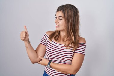 Soyutlanmış arka planda duran genç İspanyol kadın gururlu görünüyor, gülümsüyor yan tarafa baş parmak işareti yapıyor. 