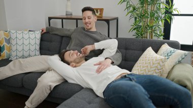 Two men couple hugging each other sitting on sofa at home