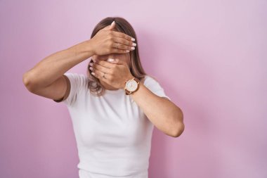 Sarışın, beyaz bir kadın pembe arka planda duruyor gözlerini ve ağzını elleriyle kapatıyor, şaşırmış ve şok olmuş. duygu gizleme 