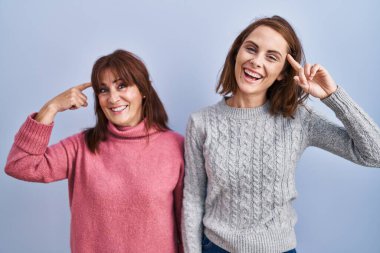 Anne ve kızı mavi arka planda durup gülümsüyor ve tek parmağıyla kafasını işaret ediyor. Harika bir fikir ya da düşünce, iyi bir hafıza. 