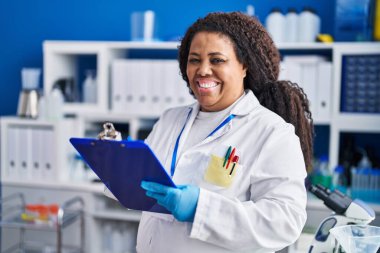 Afrikalı Amerikalı bilim kadını gülümsüyor. Laboratuardaki panoda kendinden emin bir yazı var.