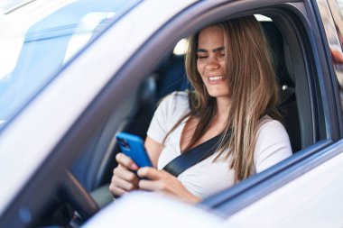 Sokakta arabada oturan akıllı telefonu kullanan genç bir kadın.