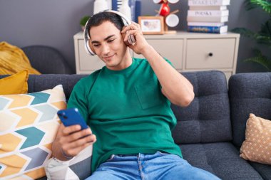 Genç İspanyol adam evdeki kanepede oturmuş müzik dinliyor.