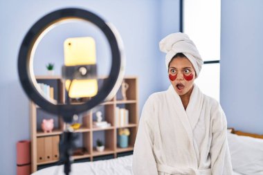 Koyu renk saçlı İspanyol bir kadın akıllı telefonuyla güzellik dersi kaydediyormuş. Şaşırmak için ağzı açık kalmış, korkmuş ve şaşırmış. 