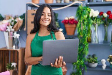 Young hispanic woman florist smiling confident using laptop at florist shop