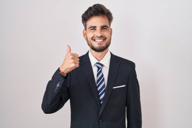 Dövmeli, takım elbiseli ve kravatlı genç İspanyol bir adam mutlu bir el hareketi yapıyor. Kameraya bakıp başarıyı gösteren ifade. 