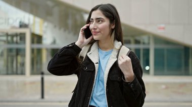 Young beautiful hispanic woman student smiling confident talking on smartphone at street