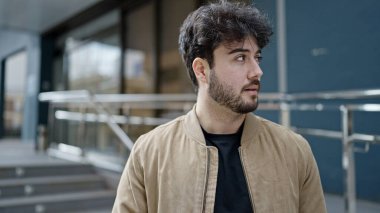 Latin kökenli genç adam ciddi bir ifadeyle sokağa bakıyor.