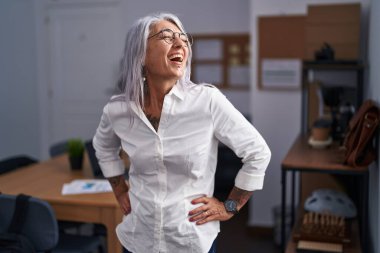 Orta yaşlı, kır saçlı, iş kadını. Ofiste kendinden emin bir şekilde gülümsüyor.