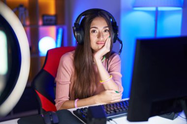 Genç İspanyol kadın video oyunları oynuyor. Kollarını kavuşturup depresyondan sıkılmış gibi görünüyor.. 