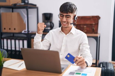 Genç İspanyol adam bilgisayarlı dizüstü bilgisayar kullanarak çalışıyor. Çok mutlu ve heyecanlı bir şekilde kollarını kaldırarak, gülümseyerek ve başarı çığlıkları atarak kazanan hareketi yapıyor. kutlama konsepti. 
