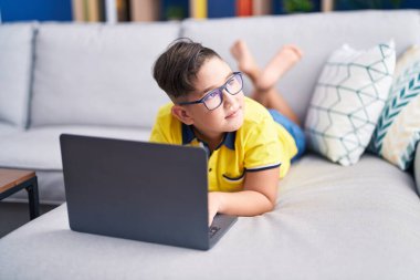 Evdeki kanepede dizüstü bilgisayar kullanan sevimli İspanyol çocuk.