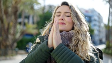 Young blonde woman praying with closed eyes at street