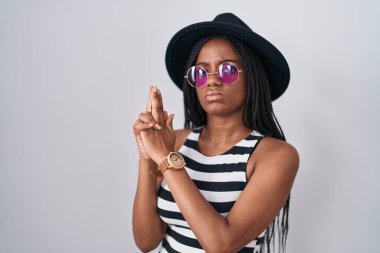 Saçları örgülü, şapka takan ve güneş gözlüklü genç Afro-Amerikalı sembolik bir silah taşıyor. El hareketleriyle cinayet silahlarıyla oynuyor, kızgın yüzlü. 