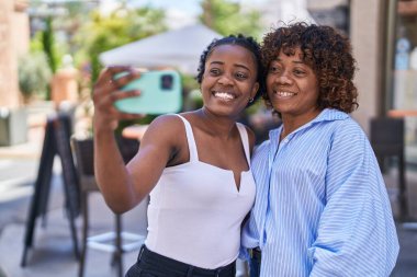 Afrika kökenli Amerikalı kadınlar anne ve kız sokakta akıllı telefonla selfie çekiyorlar.