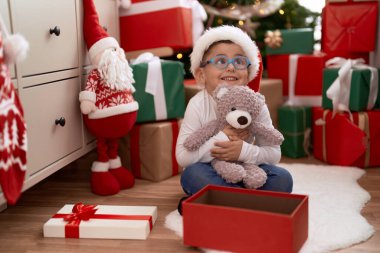 Sevimli İspanyol bebek oyuncak ayıyı kucaklıyor. Evde Noel hediyeleriyle yerde oturuyor.