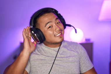 Kulaklıkla gülümseyen, kulaklık takan, dedikodu ve dedikoduları dinleyen Çinli genç bir adam. Sağırlık kavramı. 