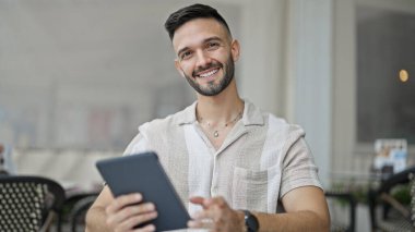 Kahve dükkanının terasında dokunmatik ped kullanarak gülümseyen İspanyol genç adam.