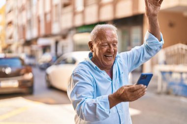 Senior grey-haired man using smartphone with cheerful expression at street