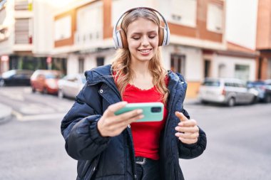 Sokakta video oyunu oynarken kendine güvenen genç sarışın kadın.