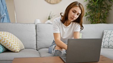 Evdeki kanepede dizüstü bilgisayar kullanan genç bir kadın.