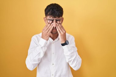 Sarı arka planda duran İspanyol genç adam yorgunluk ve baş ağrısı için gözlerini ovuşturuyor, uykulu ve yorgun ifade. görme sorunu 