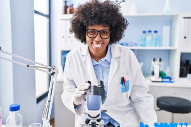 African american woman scientist smiling confident using microscope at laboratory