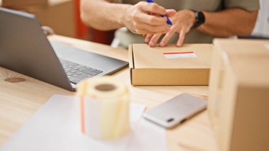 Latin kökenli genç bir iş adamı ofisteki dizüstü bilgisayarla paket üzerine yazıyor.