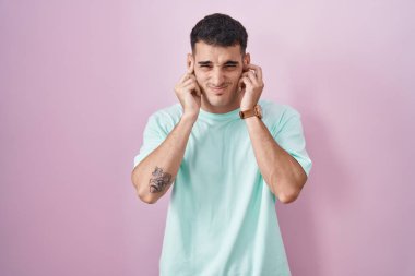 Pembe arka planda duran yakışıklı İspanyol adam yüksek sesli müzik sesi için parmaklarıyla kulaklarını kapatıyor. sağır kavramı. 