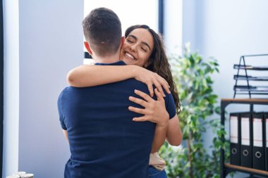 Young hispanic couple business workers hugging each other standing at office