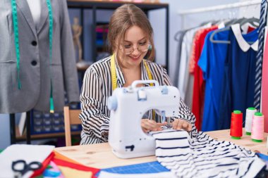 Terzide dikiş makinesi kullanan kendine güvenen genç sarışın kadın terzi.