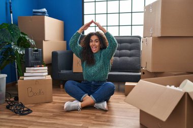 Genç İspanyol kadın, yeni evinde yerde oturuyor. Komik bir ifadeyle dilini dışarı çıkarıyor.. 