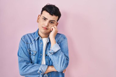 Pembe arka plan üzerinde duran ikili olmayan kişi kollarını kavuşturarak depresyon sorunlarından yorgun ve sıkılmış göründüğünü düşünüyor.. 